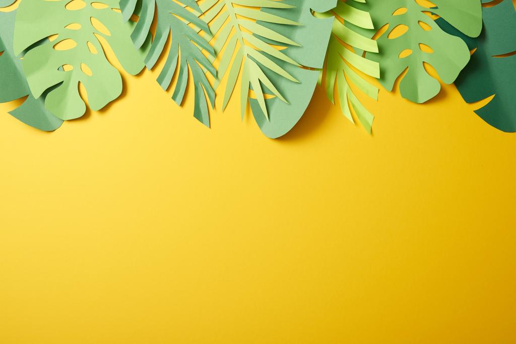 Draufsicht auf Papier geschnittene grüne Palmblätter auf gelbem Hintergrund mit Kopierraum - Foto, Bild