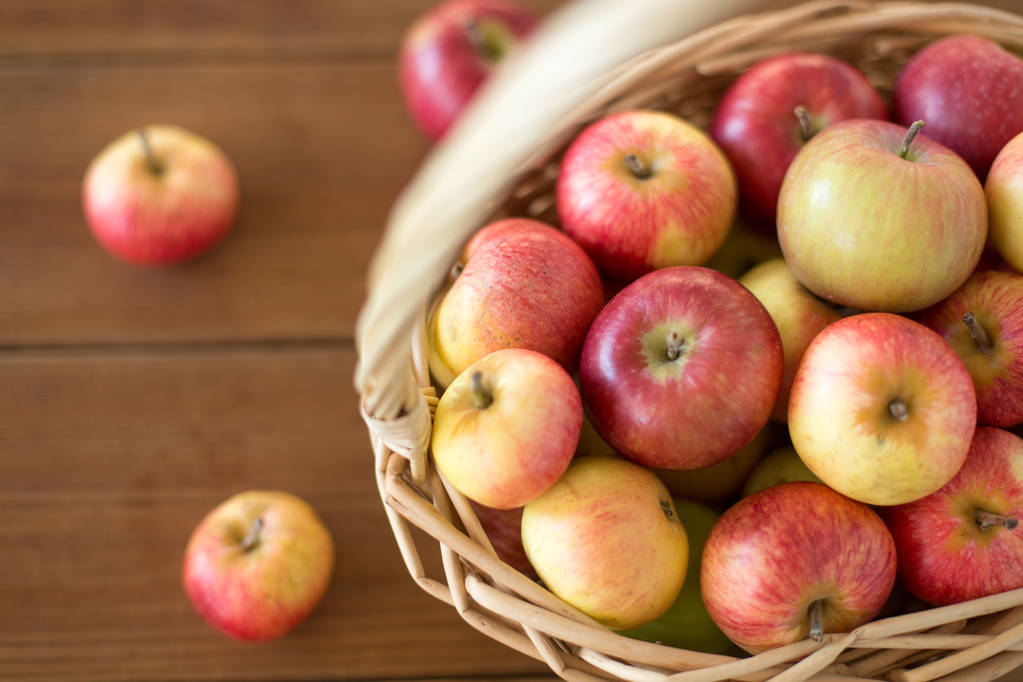 reife Äpfel im Weidenkorb auf Holztisch - Foto, Bild