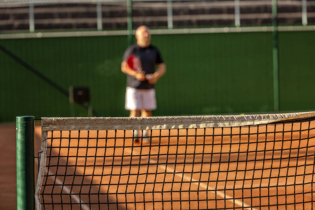Un calvo de mediana edad juega al tenis en la cancha al aire libre. Día soleado. Desenfoque
. - Foto, imagen