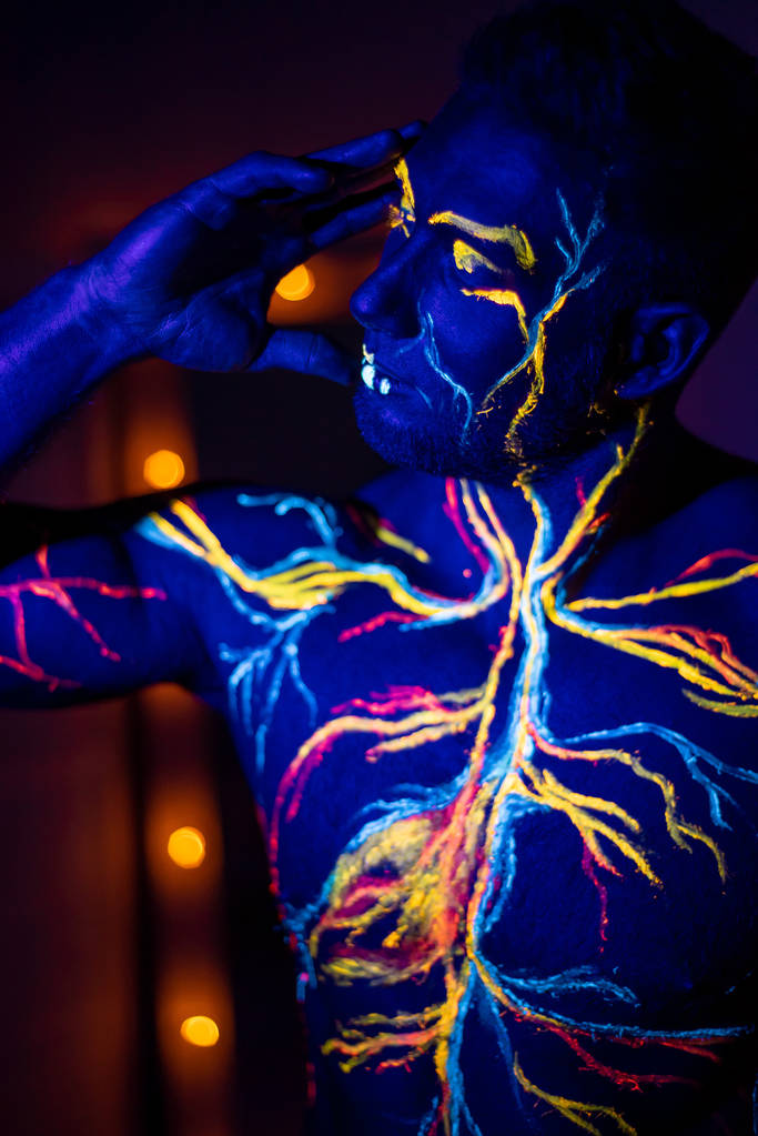 Los patrones UV arte corporal del sistema circulatorio en el cuerpo de un hombre. En el torso de un atleta muscular, las venas y arterias se dibujan con tintes fluorescentes. Culturista parado junto al espejo con lámparas
. - Foto, Imagen