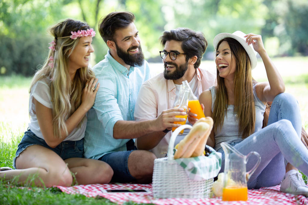 Onnellisia nuoria ystäviä puistossa ottaa piknik aurinkoisena päivänä
. - Valokuva, kuva