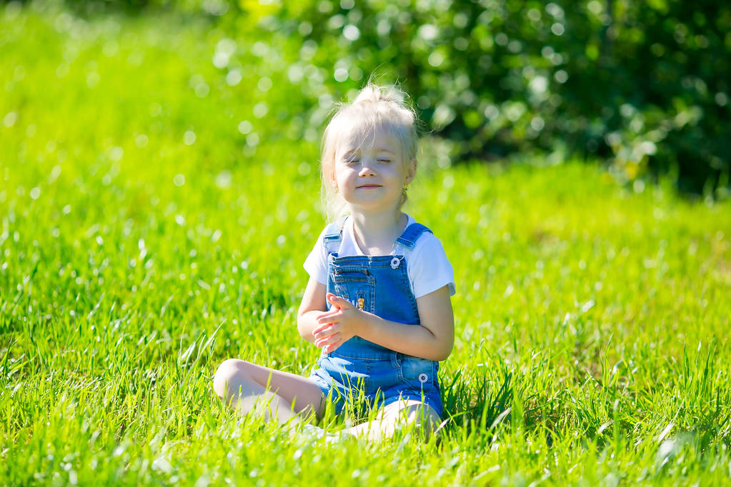 Блондинка, 4-5 лет, сидит в позе йоги, занимается спортом и медитацией в парке на траве
. - Фото, изображение