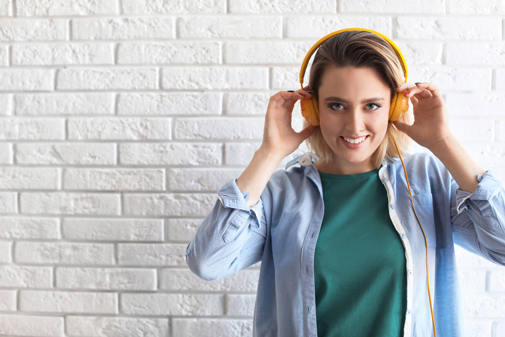 Portrait of beautiful woman listening to music with headphones near brick wall. Space for text - Photo, Image