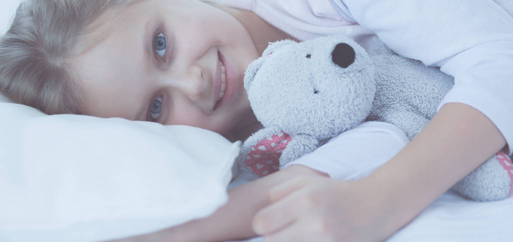 kind meisje slaapt in het bed met een speeltje teddy beer. - Foto, afbeelding