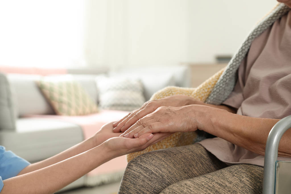 Enfermeira segurando as mãos da mulher idosa dentro de casa, fechar com espaço para texto. Assistência aos idosos
 - Foto, Imagem