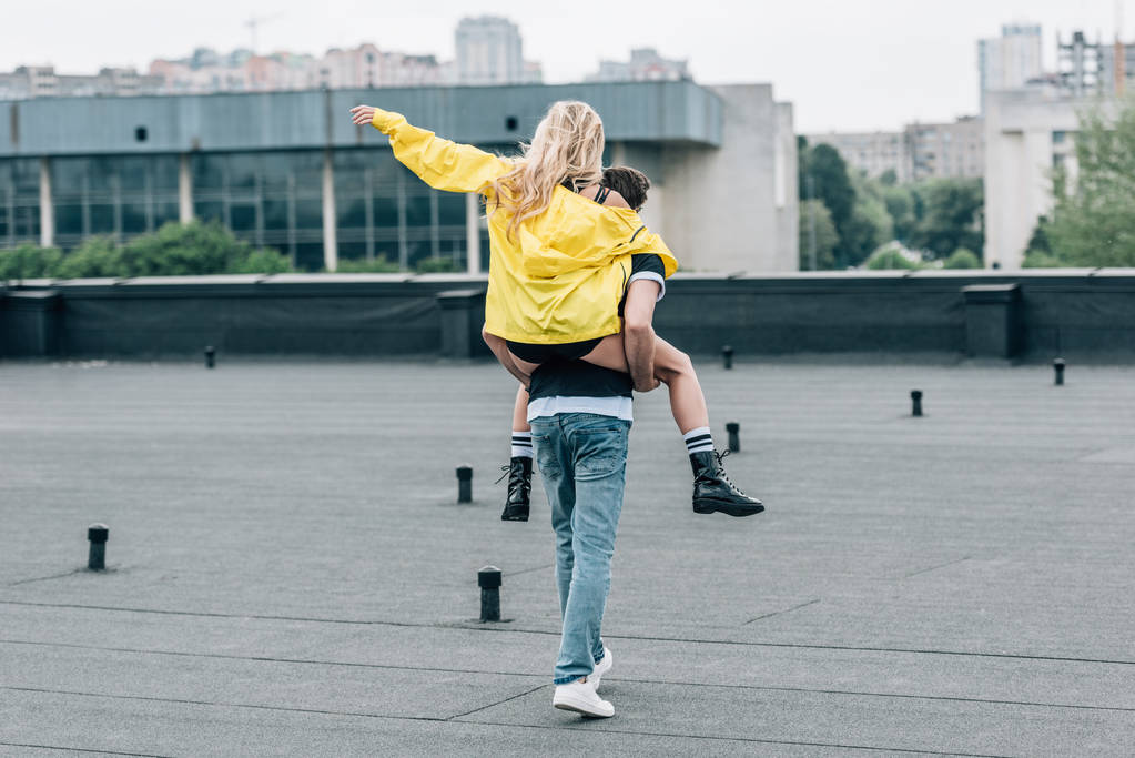 вид ззаду жінки в жовтій куртці, що грає з чоловіком на даху
  - Фото, зображення