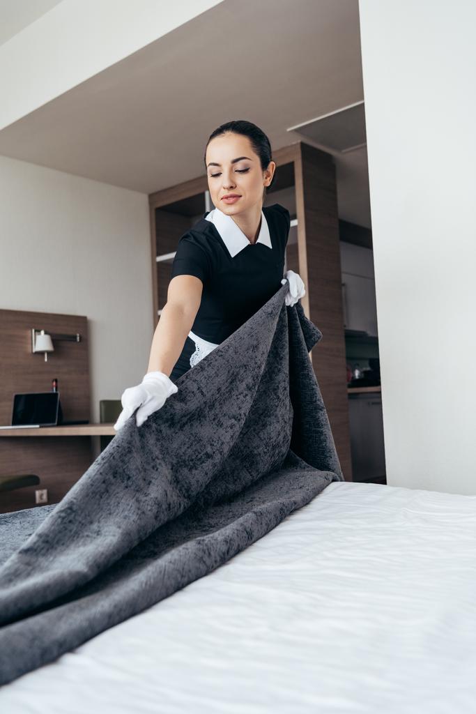 bonita criada en guantes blancos limpieza cama en habitación de hotel
 - Foto, imagen