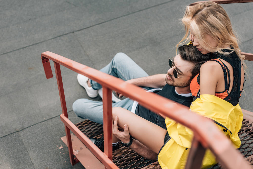 ξανθιά γυναίκα και όμορφος άντρας σε γυαλιά αγκάλιασμα και κάθεται στις σκάλες  - Φωτογραφία, εικόνα