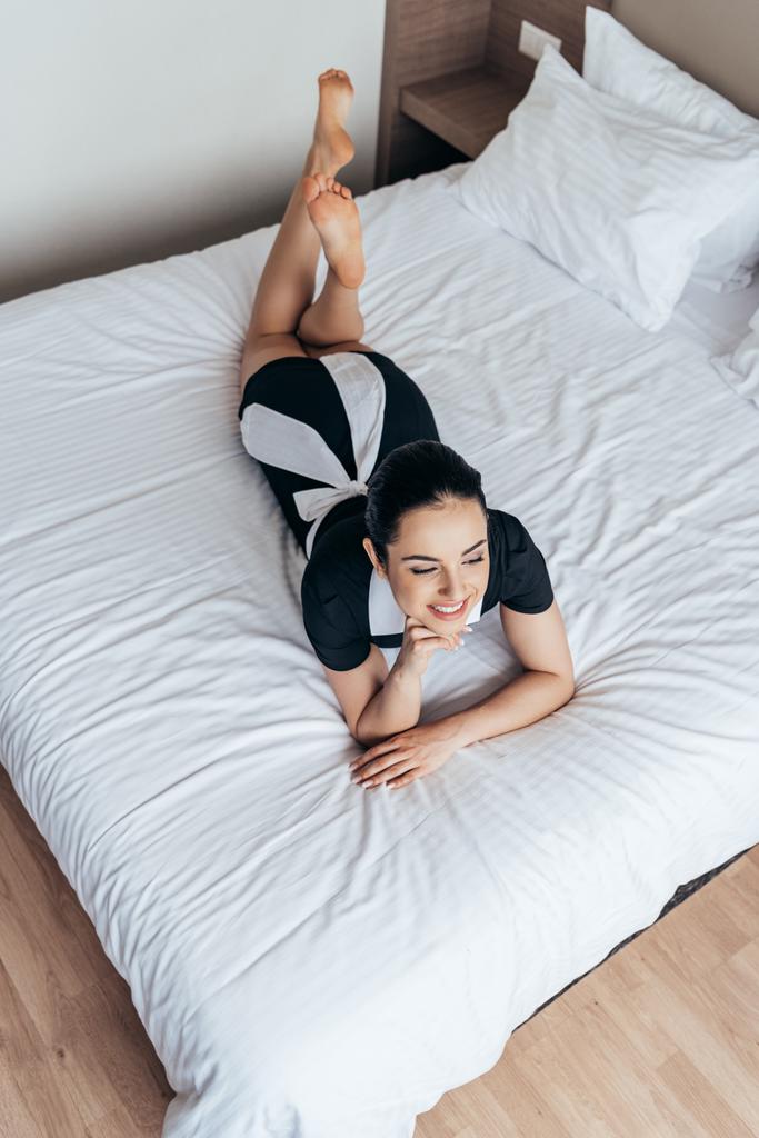 Režie na usmívající se bosou služebnou ležící na posteli v hotelovém pokoji - Fotografie, Obrázek