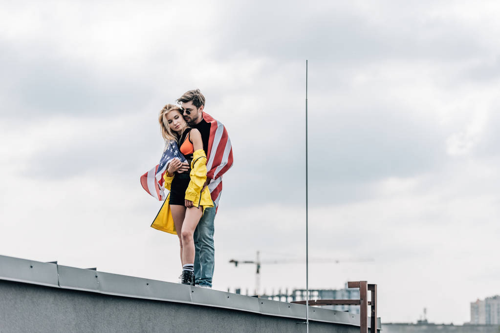 mulher atraente e homem bonito com bandeira americana abraçando no telhado
  - Foto, Imagem