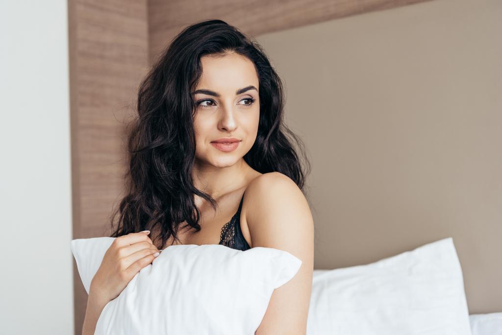 σέξι νεαρή γυναίκα σε εσώρουχα κρατώντας λευκό μαξιλάρι στο υπνοδωμάτιο - Φωτογραφία, εικόνα