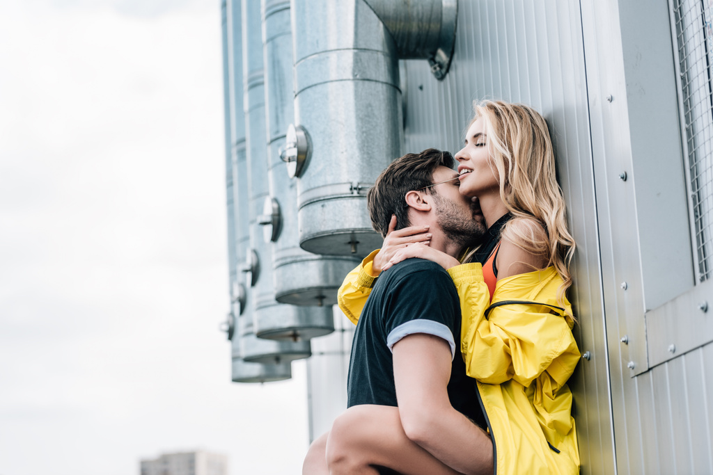 muž v tričku a atraktivní žena líbání a objetí na střeše  - Fotografie, Obrázek
