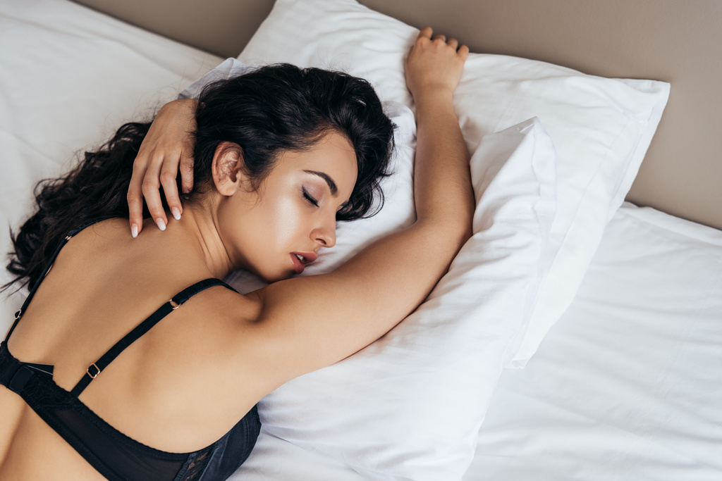 αισθησιακό μελαχρινή νεαρή γυναίκα σε μαύρο σουτιέν κοιμάται στο κρεβάτι - Φωτογραφία, εικόνα