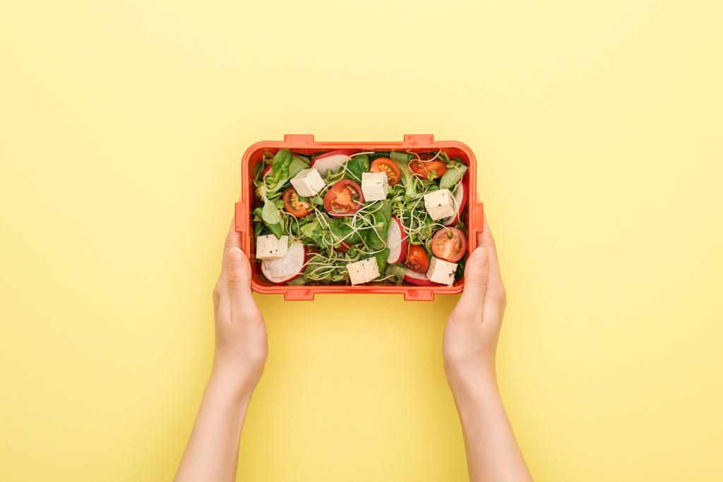 sarı arka plan üzerinde elinde salata ile öğle yemeği kutusu tutan kadın kırpılmış görünümü - Fotoğraf, Görsel
