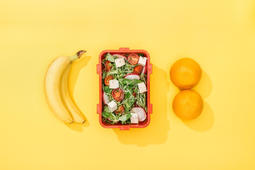 Ansicht der Lunchbox mit Salat in der Nähe von Bananen und Orangen - Foto, Bild