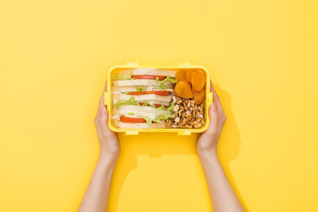abgeschnittene Ansicht einer Frau mit Lunchbox mit Nüssen, getrockneten Aprikosen und Sandwiches in Frauenhänden - Foto, Bild
