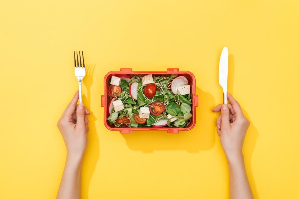 サラダ付き弁当箱の上にフォークとナイフを持つ女性のトリミングビュー - 写真・画像