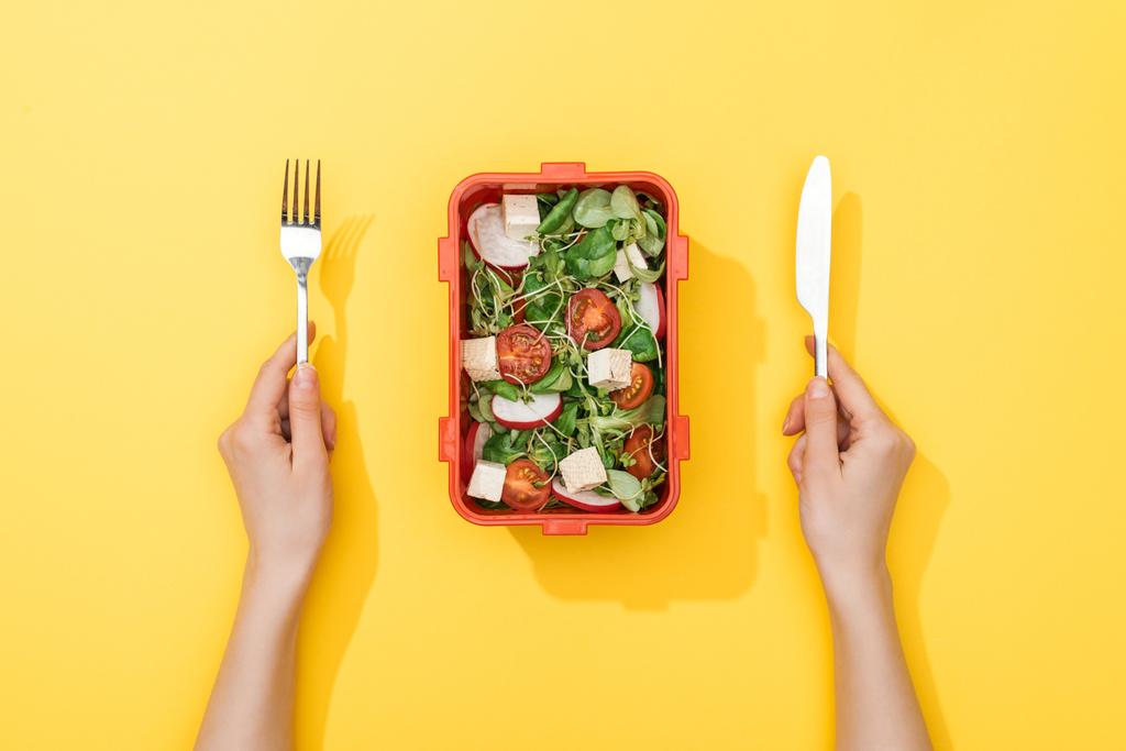 vue recadrée de la femme tenant fourchette et couteau sur la boîte à lunch avec salade
 - Photo, image