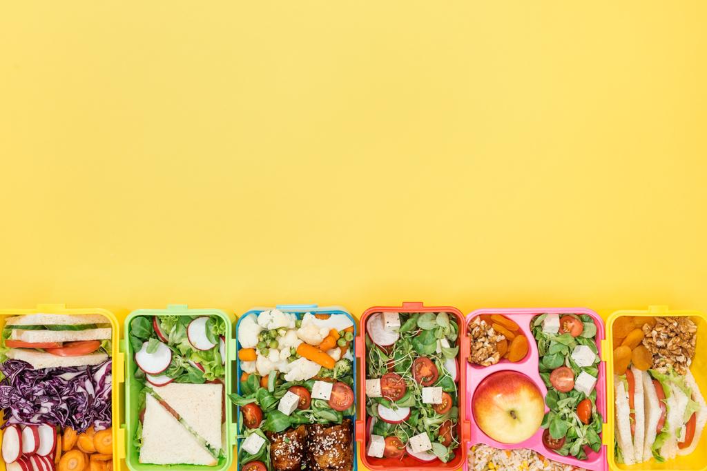 Κορυφαία θέα των κουτιών μεσημεριανού γεύματος με φαγητό σε κίτρινο φόντο με χώρο αντιγραφής - Φωτογραφία, εικόνα