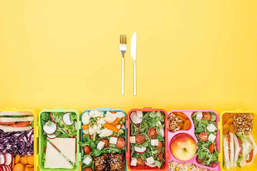 bovenaanzicht van de vork en het mes in de buurt van lunchboxen met voedsel - Foto, afbeelding