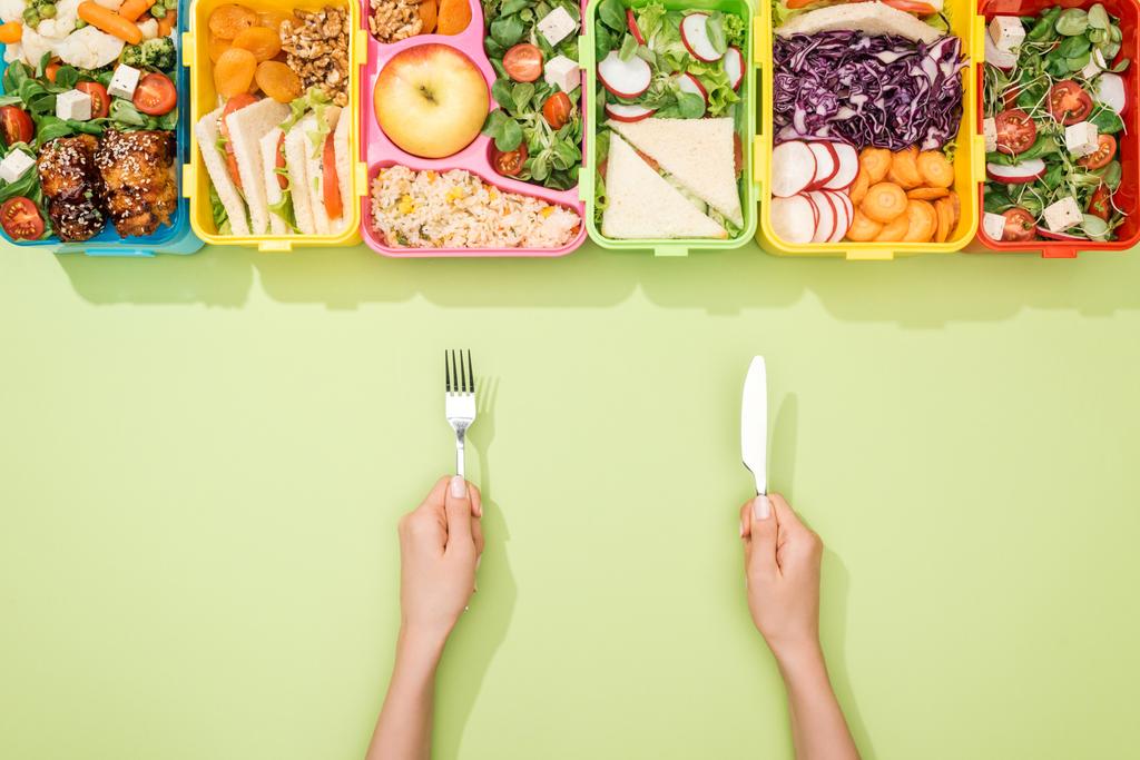 Ausgeschnittene Ansicht einer Frau mit Gabel und Messer in der Nähe von Lunchpaketen mit Lebensmitteln - Foto, Bild