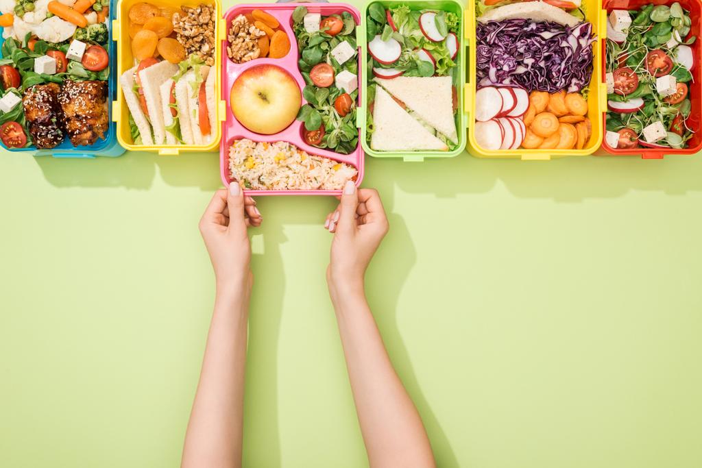 緑の背景に食べ物を持つ弁当を選ぶ女性のトリミングビュー - 写真・画像