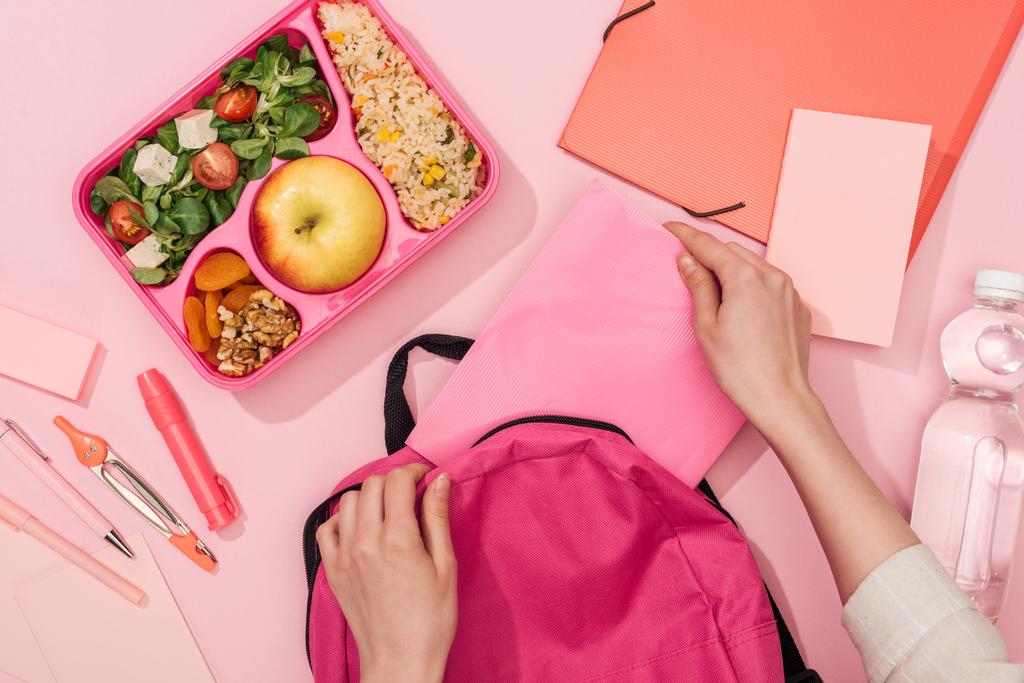 vista cortada da mochila de embalagem da mulher perto da caixa de almoço com alimentos e artigos de papelaria
 - Foto, Imagem