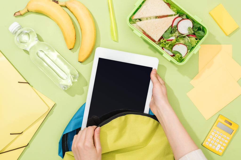 vágott kilátás nő csomagolás digitális tabletta a hátizsákban közelében ebéd doboz, banán, üveg víz és irodaszerek - Fotó, kép