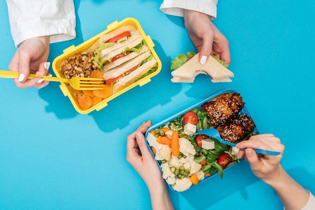 Ausgeschnittene Ansicht von zwei Frauen, die Gabeln über Lunchboxen mit Lebensmitteln halten - Foto, Bild
