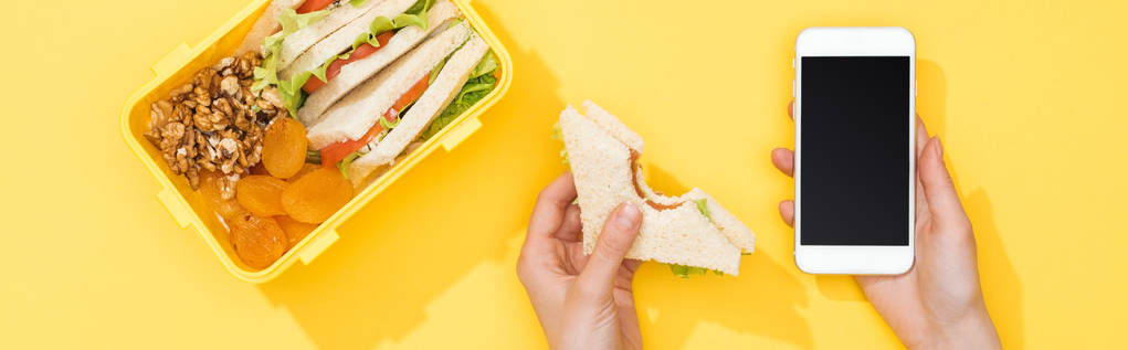 vista cortada de mulher segurando sanduíche e smartphone perto com comida
 - Foto, Imagem