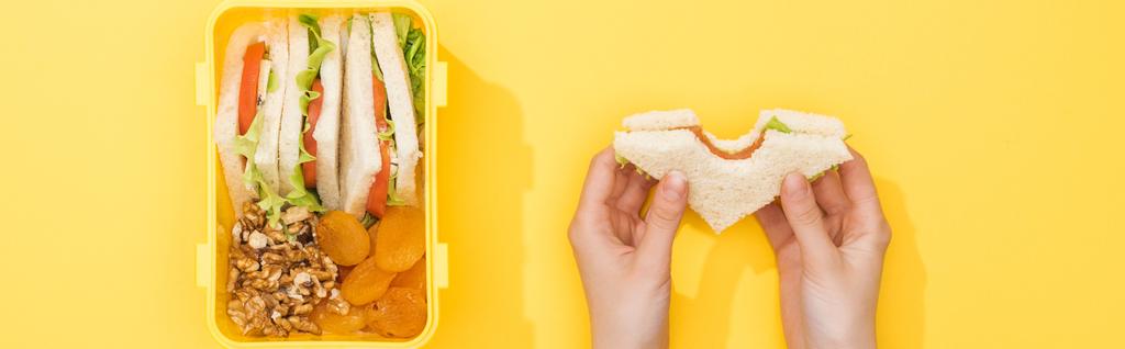 abgeschnittene Ansicht einer Frau mit Sandwich in der Hand in der Nähe von Lunchbox mit Lebensmitteln - Foto, Bild