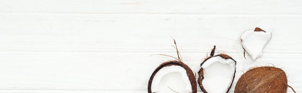 bovenaanzicht van kokos helften op wit houten oppervlak, panoramische foto - Foto, afbeelding