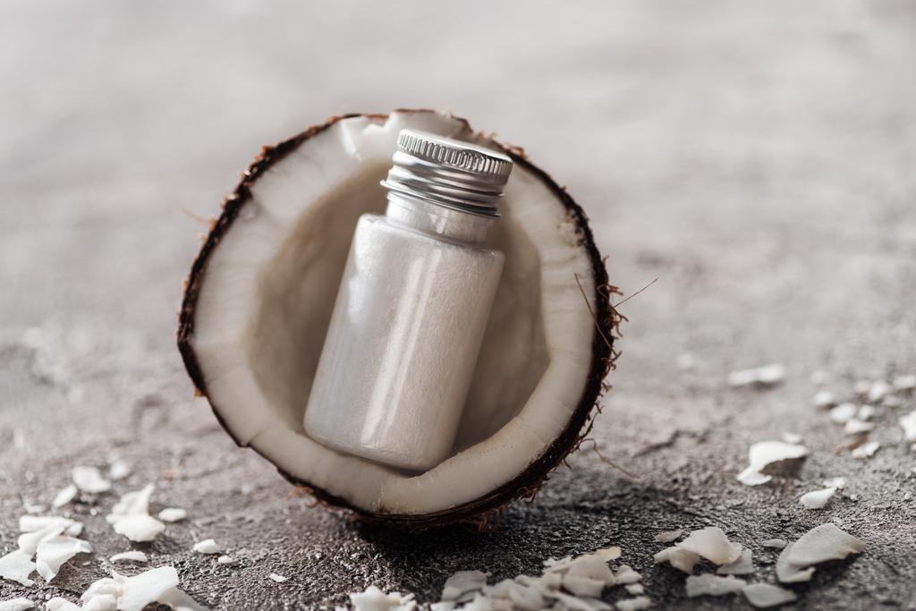 láhev s bílým kokosovým krémem v kokosové půlce na šedé, texturované pozadí - Fotografie, Obrázek