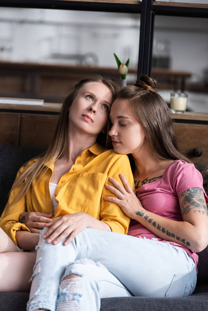 twee mooie lesbiennes omarmen terwijl zittend op de Bank in de woonkamer - Foto, afbeelding