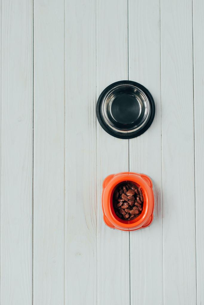 верхний вид миски с кормом для домашних животных и пустой миской на деревянной поверхности
 - Фото, изображение