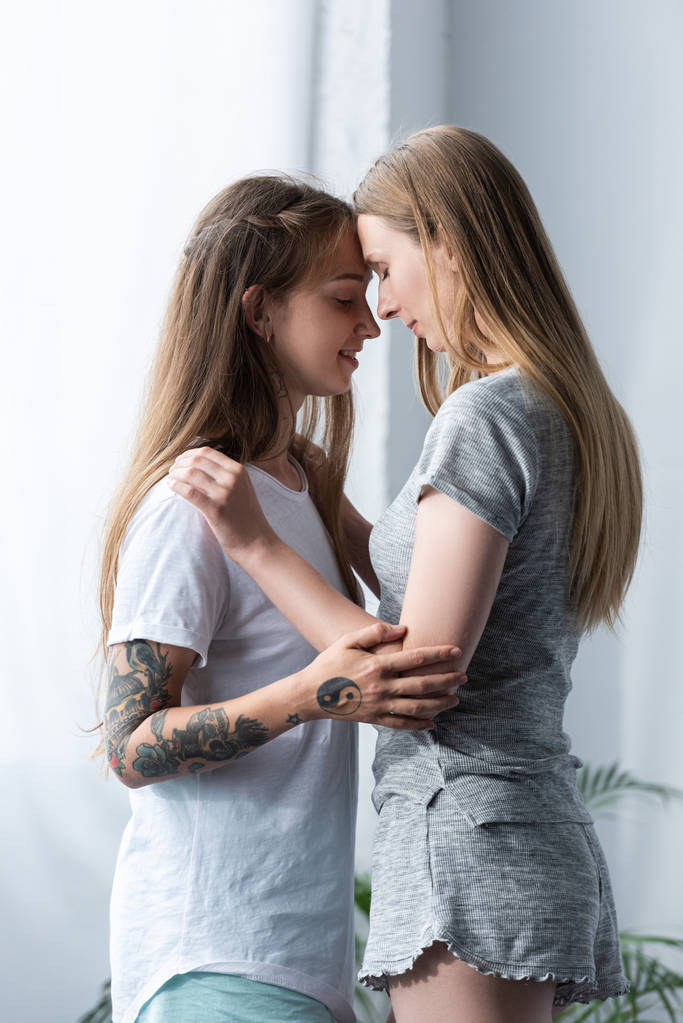 yatak odasında kucaklayan t-shirt iki gülümseyen lezbiyenler - Fotoğraf, Görsel
