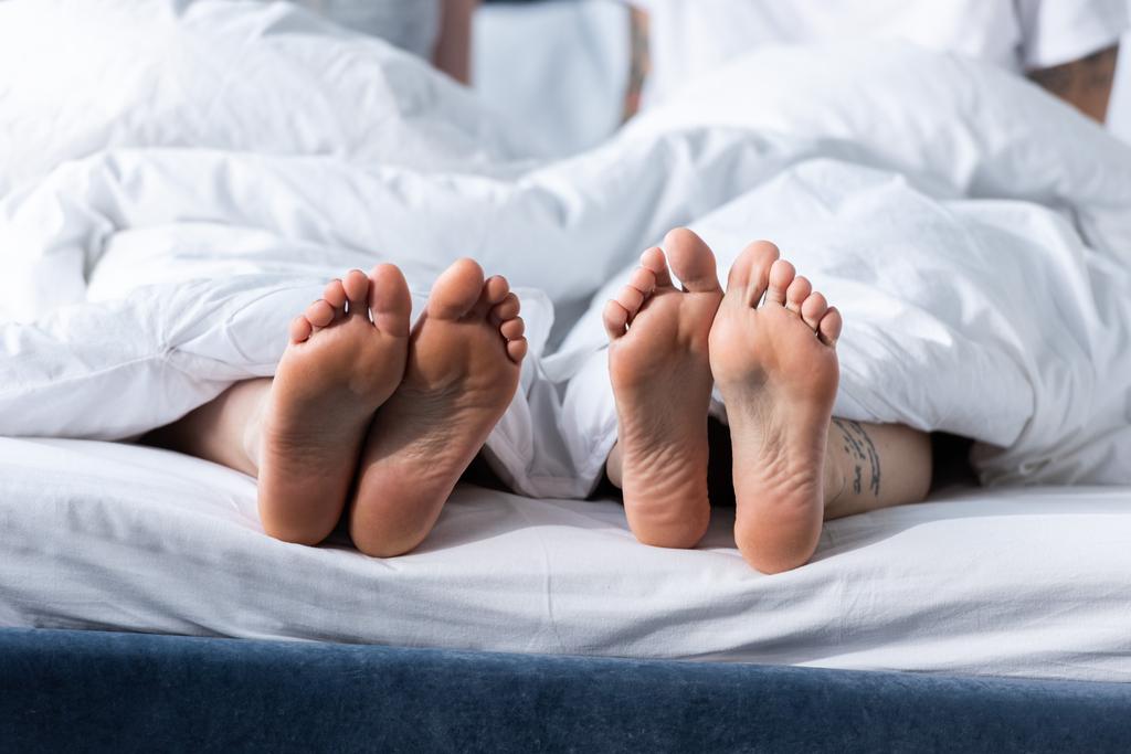 vista parcial de dois descalços lésbicas deitado sob cobertor
 - Foto, Imagem