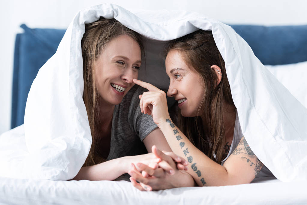 due lesbiche felici che si tengono per mano mentre si trovano sotto la coperta sul letto
 - Foto, immagini