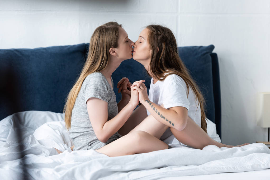 vue latérale de deux lesbiennes tenant la main et s'embrassant sur le lit
 - Photo, image