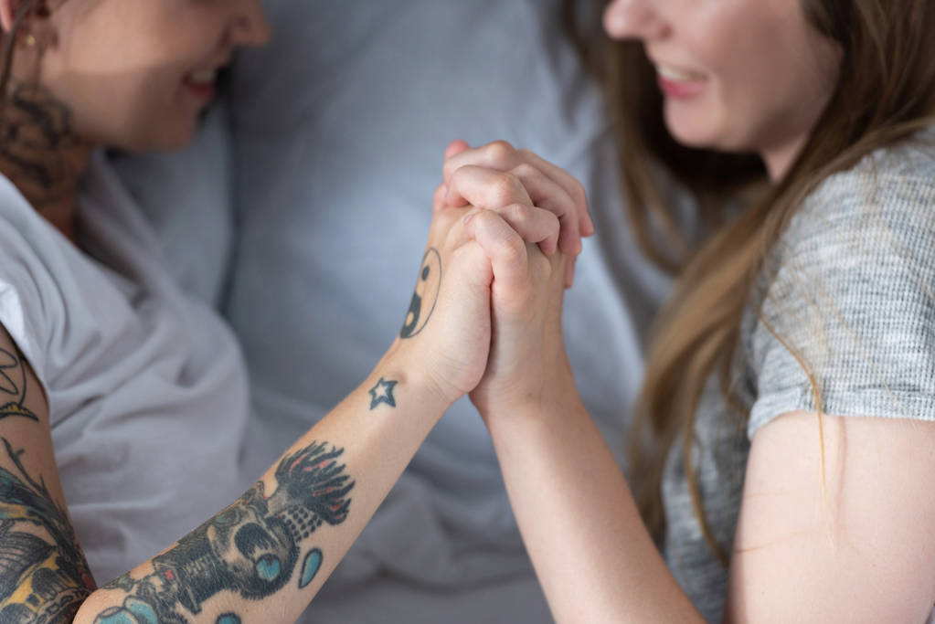 cropped view of two lesbians holding hands while lying in bed - Photo, Image