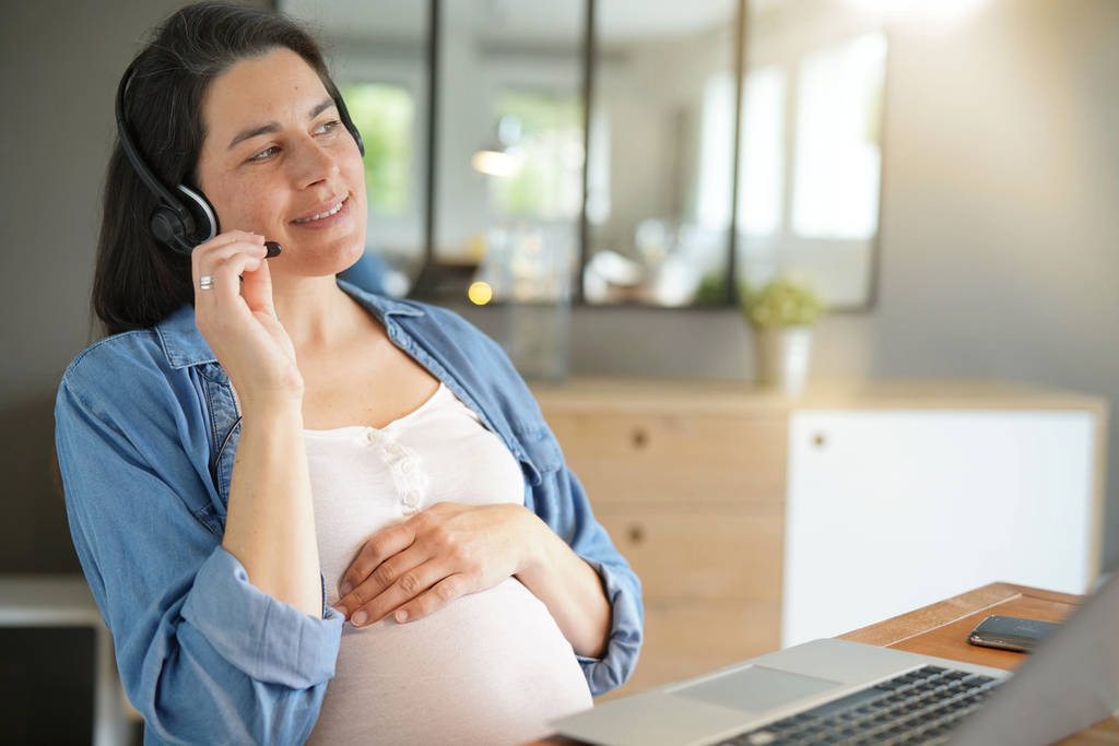 Pregnant woman working from home with laptop and headset - Photo, Image