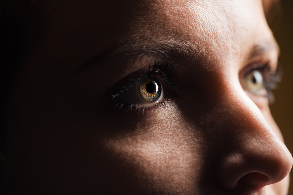 Close-up van de volwassen vrouw oog met wimpers en wenkbrauw op zoek in het donker - Foto, afbeelding