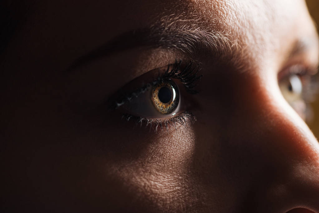 κοντινό εικόνα της ενήλικης γυναίκας μάτι κοιτάζοντας μακριά στο σκοτάδι - Φωτογραφία, εικόνα