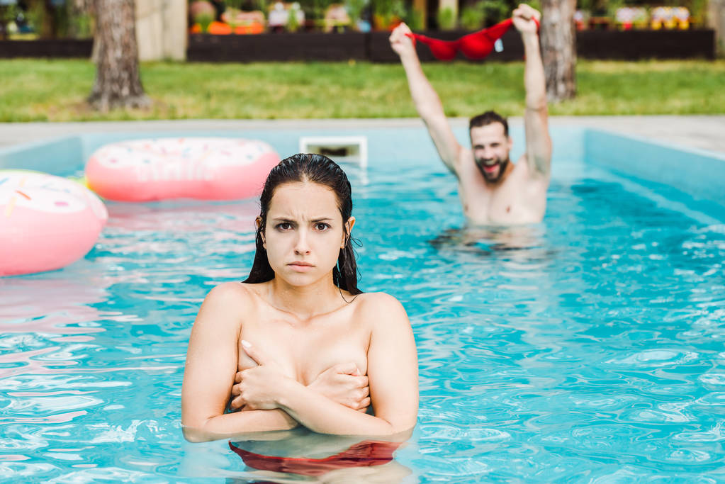 selective focus of woman covering breasts in swimming pool near man  - Photo, Image