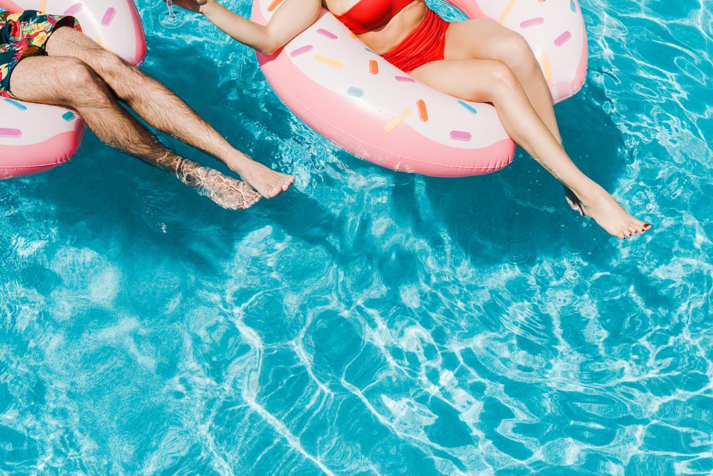 cropped view of man and woman with barefoot on pink inflatable rings in swimming pool  - Photo, Image