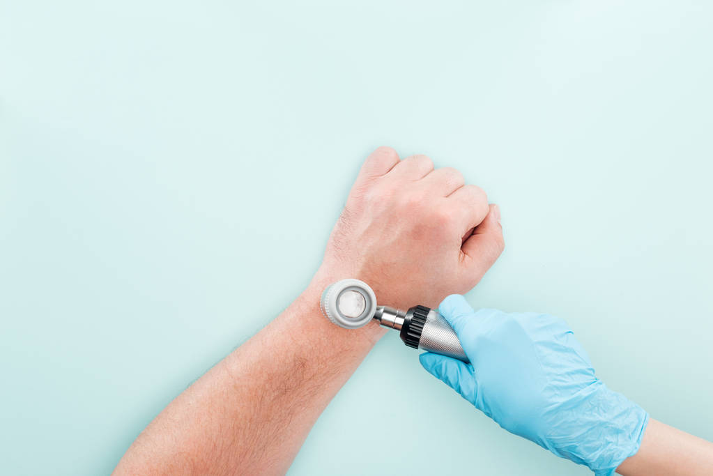 vágott kilátás orvos vizsgálata az ember keze a dermatoscope izolált kék - Fotó, kép