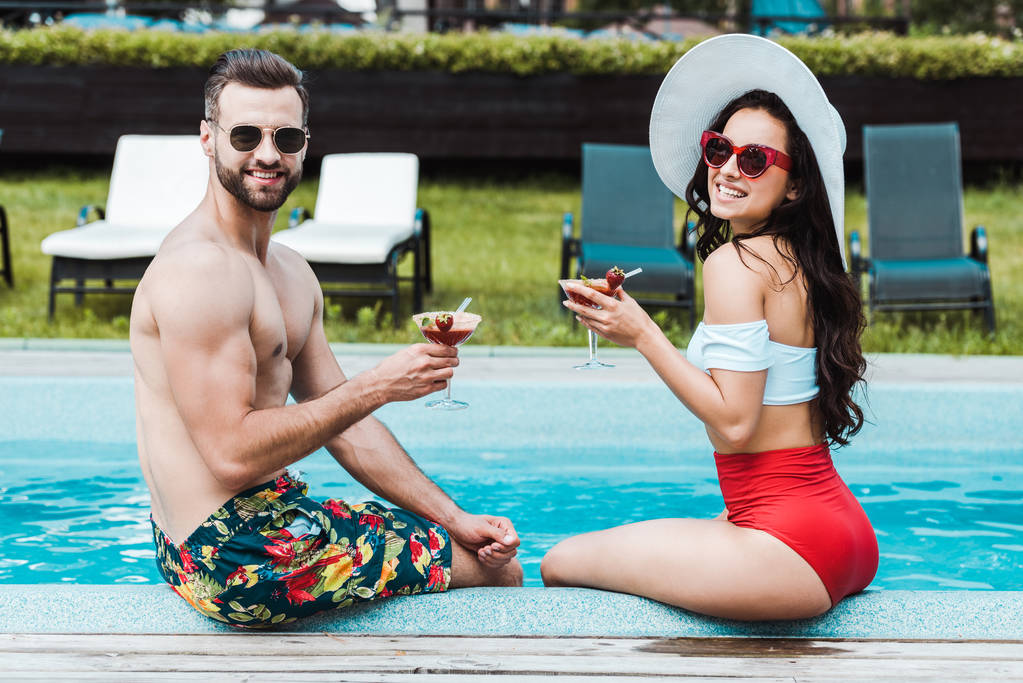 счастливый мужчина в солнечных очках, держащий коктейльные очки с женщиной в соломенной шляпе
  - Фото, изображение