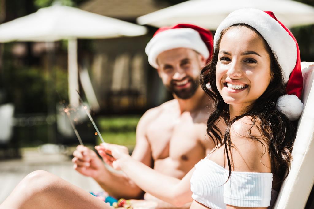 selective focus of happy woman in santa claus hat and man holding sparklers  - Photo, Image