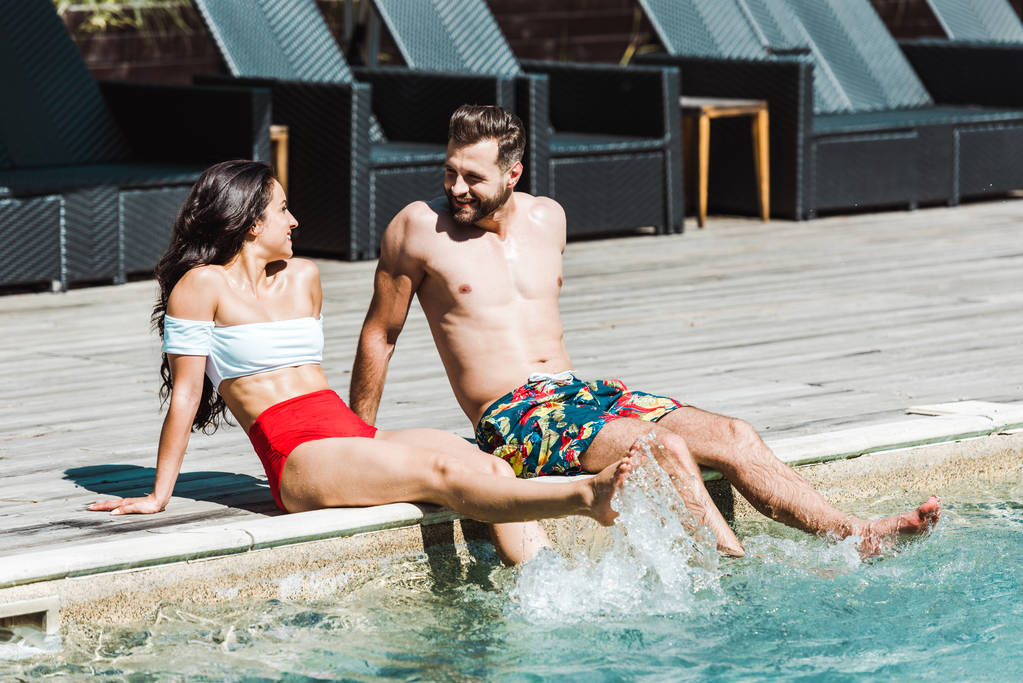 hombre feliz mirando a la mujer mientras está sentado en cubiertas de madera cerca de la piscina
  - Foto, imagen
