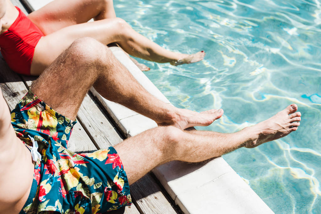 cropped view of man and woman sitting on wooden decks near swimming pool  - Photo, Image